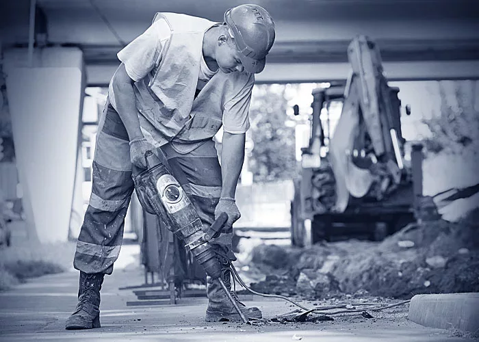 Ein Bauhelfer mit einem Schlagbohrer bei der Arbeit.